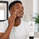Man applying after-shave to his face with a bottle of Shave Essentials LLC product in the foreground.