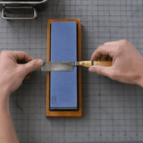 Person sharpening a Damascus Straight Razor on a whetstone with a grid background