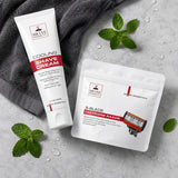 A tube of SHAVE Essentials Cooling Shave Cream and a pouch of SHAVE Essentials 5-Blade Cartridge Razor arranged on a light gray stone surface with water droplets, green mint leaves, and a dark gray towel.