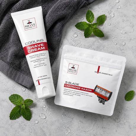 A tube of SHAVE Essentials Cooling Shave Cream and a pouch of SHAVE Essentials 5-Blade Cartridge Razor arranged on a light gray stone surface with water droplets, green mint leaves, and a dark gray towel.