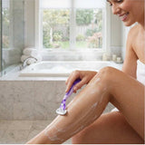 Woman shaving her leg with a purple razor in a bathroom. - Shave Essentials